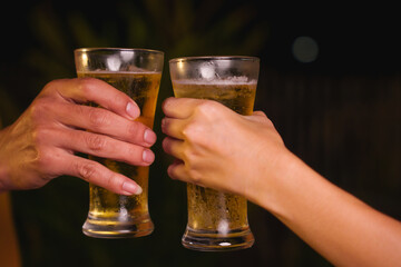 Close-up of friends clinking glasses of beer, celebrating together at a bar.The lively atmosphere captures laughter, camaraderie,good times, as young friends enjoy a night out with refreshing drinks