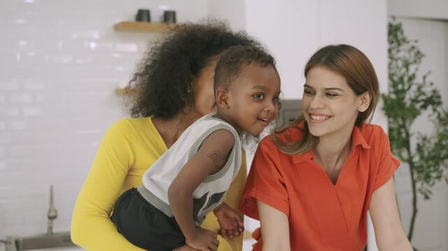 Family of happy interracial lesbian couple and her black cute son standing smiling and playing together having fun and cheerful in the kitchen room at home. Female black and white LGBTQ pride concept.