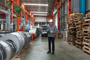 A worker dressed in hardhat and  protective glove, stand in a factory checks materials while...