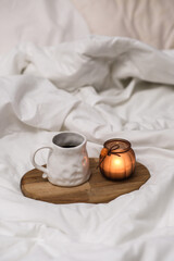 Wooden tray with coffee and interior decor on the bed with white linen