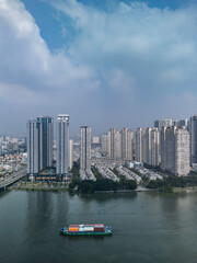 Fototapeta premium Freighter with containers on river against background of modern high rise and villas in new residential area with dramatic sky.