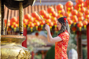 Asian woman in red cheongsam qipao dress is offering incense to the ancestral god inside Chinese Buddhist temple during lunar new year for  for best wish blessing and good luck