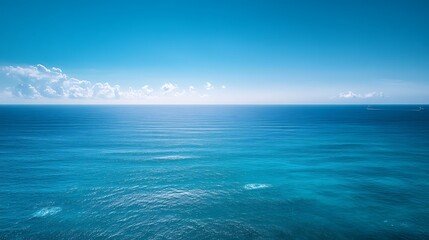 A vast, tranquil ocean stretches under a bright blue sky, reflecting sunlight across the serene water surface.