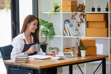 Beautiful business woman Happy working online shopping at her store. Through phone, computer, young woman seller prepares parcel boxes to send to customers. online sales ecommerce
