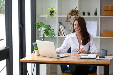 Beautiful business woman Happy working online shopping at her store. Through phone, computer, young woman seller prepares parcel boxes to send to customers. online sales ecommerce