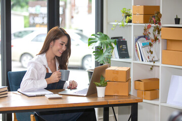Beautiful business woman Happy working online shopping at her store. Through phone, computer, young woman seller prepares parcel boxes to send to customers. online sales ecommerce
