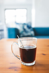 hand holding coffee in clear mug in front of blurred home interior background, habits and lifestyle concept