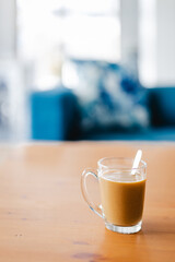 hand holding coffee in clear mug in front of blurred home interior background, habits and lifestyle concept