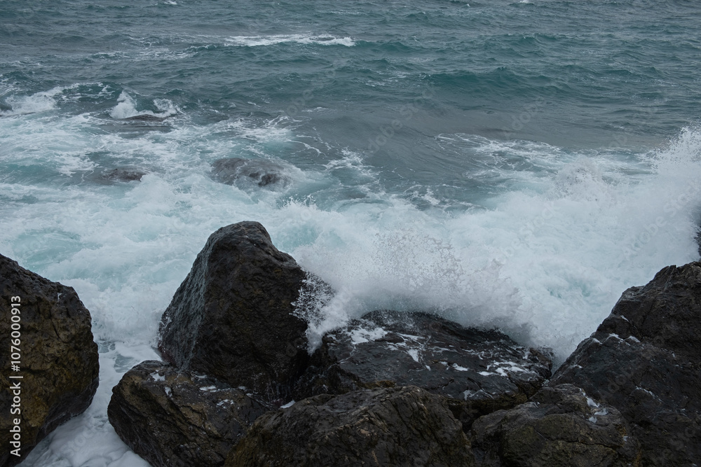 Wall mural Turquoise sea stone beach, breaking waves on a cloudy spring day. Beautiful sea background. The concept of summer, vacation, travel. The purest clear sea water, large stones on the beach close-up