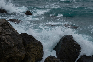 Turquoise sea stone beach, breaking waves on a cloudy spring day. Beautiful sea background. The concept of summer, vacation, travel. The purest clear sea water, large stones on the beach close-up