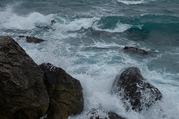 Turquoise sea stone beach, breaking waves on a cloudy spring day. Beautiful sea background. The concept of summer, vacation, travel. The purest clear sea water, large stones on the beach close-up