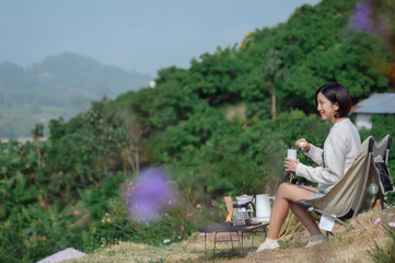 A woman enjoying coffee at a picturesque mountain campsite with an outdoor coffee station