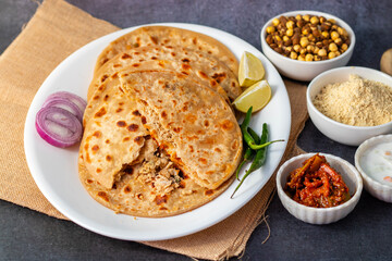 Sattu paratha, a spiced chickpea flour-stuffed flatbread, served hot with tangy pickle and cool, creamy raita for a flavorful meal.