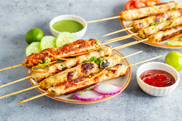 Juicy chicken seekh kababs, grilled to perfection, served with refreshing mint chutney and tangy tomato sauce for a flavorful meal.