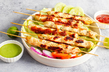 Juicy chicken seekh kababs, grilled to perfection, served with refreshing mint chutney and tangy tomato sauce for a flavorful meal.