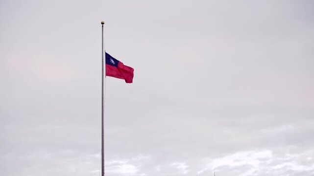 The Taiwan flag waving high on a tall pole, set against a cloudy sky, evoking a sense of patriotism and pride in Taiwan&sbquo; independence.