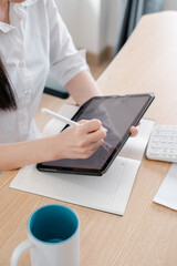 A woman uses a stylus on a digital tablet at a desk, showcasing modern technology in a professional setting.