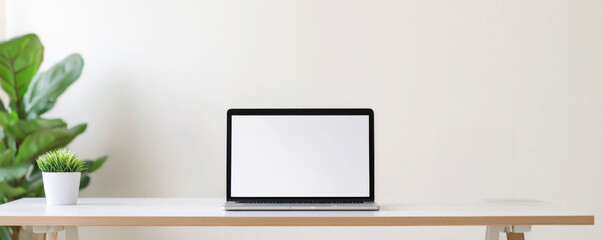 Obraz premium Modern laptop on a minimalistic desk with a potted plant and a blank screen.
