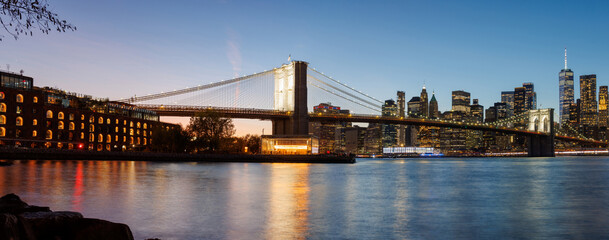 A panoramic sunset view of the Brooklyn Bridge stretching towards Manhattan