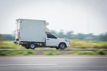 Motion blurred image, of a small white truck for road logistics, Side view of a pickup truck driving on a country road, Truck running on the road, Small truck on the road.