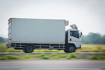 Motion blurred image, of a small white truck for road logistics, Side view of a small truck driving on a country road, Truck running on the road, Small truck on the road.