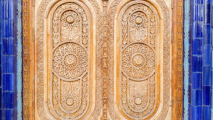 Ornate Wooden Door with Intricate Carvings Surrounded by Blue Tile