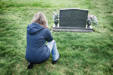 Grieving woman kneels in from of tombstone.