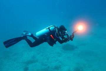 Obraz premium Scuba diver videographer exploring underwater seascape in the ocean. Scuba diving trip, travel photo and diver. Deep sea, diver videographer with lights and relaxation while scuba diving.