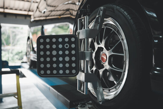 Closeup of car wheel alignment at auto repair center. Vehicle maintenance service in an automotive workshop with mechanical equipment for tire balance and adjustment.