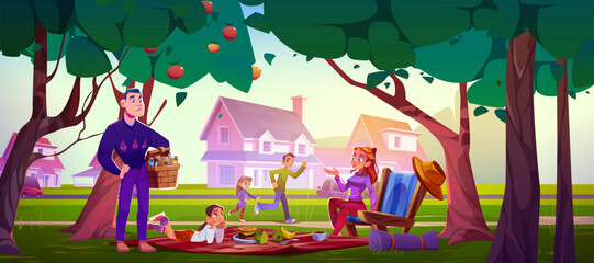 Family enjoying outdoor picnic beneath apple trees in suburban park. Parents with three children spread blanket near houses. Father holds wicker basket, mother rests in chair, kids playing around.