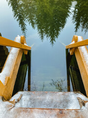 A beautifully crafted wooden bridge gracefully spans over a serene body of water, with lush trees casting their reflections gently upon the surface of the calm water below