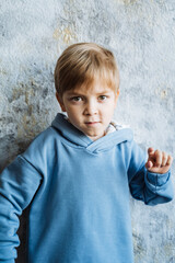 A young boy donned in a bright blue hoodie is standing in front of a wall, possibly admiring his surroundings or simply enjoying the moment and feeling a sense of happiness and joy