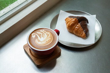Hot coffee latte with latte art milk foam a swan shape in cup mug with chocolate Croissant on wood desk on top view.As breakfast In a coffee shop at the cafe,during business work concept,Rainy season