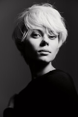 Confident young woman with short white hair posing in moody black and white lighting, showcasing a strong, expressive look. Artistic portrait concept.