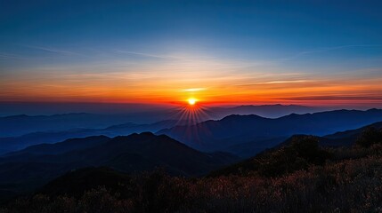 Fototapeta premium Stunning sunset in the mountains, creating a breathtaking blend of orange and blue skies. Perfect for capturing the serene beauty of sunsets in the mountains with ample copy space.