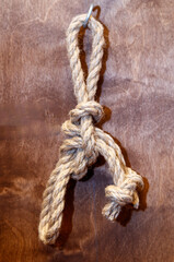 A rope is tied in a knot and is hanging from a wooden surface