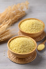 Organic yellow millet grain in wooden bowl with spoon on white table, Healthy food ingredient