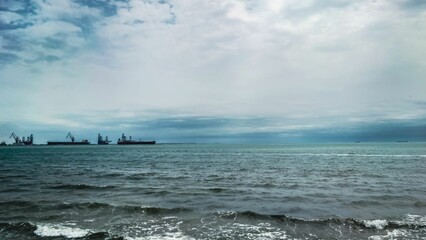 Calm sea with distant cargo ships under cloudy sky.