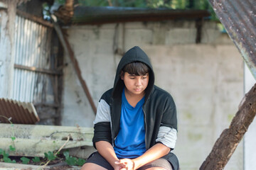Asian teenage boy in a black t-shirt and coat stood and sat in a secret place with a sad expression...