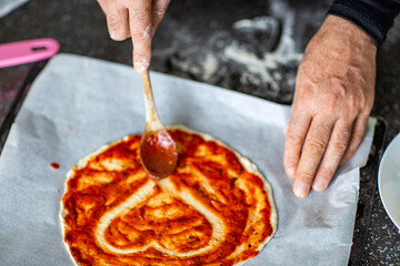 Person adding tomato sauce to pizza heart shaped