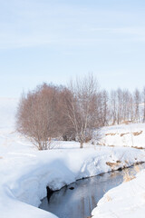 Tranquil winter landscape with a winding stream and snow-covered banks
