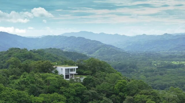 An aerial view reveals a stunning modern house in the lush forests of Costa Rica, surrounded by mountains, ideal for nature lovers and outdoor enthusiasts seeking adventure and tranquility