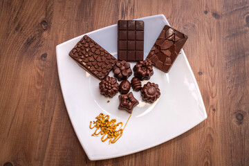 A selection of artisanal chocolate bars and decorative chocolate pieces arranged on a white plate with a touch of pistachio garnish, set against a rustic wooden background.