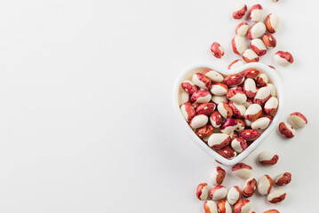 Heart shape  bowl with red and white kidney beans and scattered  on white background  top view whith copy space