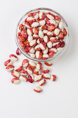Glass bowl with red and white  kidney beans scattered  on white background isolated, top view