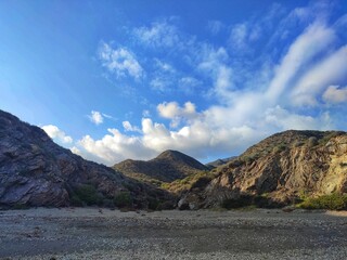 Rocky hills and a valley under a bright blue sky with scattered clouds