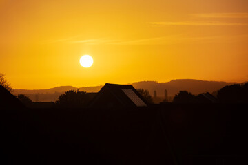 Golden orange sunrise silhouette over suburbs with roof top and trees