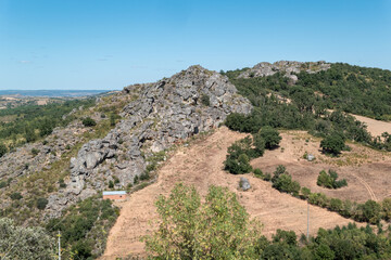 Paisagem montanhosa com grandes formações rochosas, em meio a um campo rural, sob um céu azul