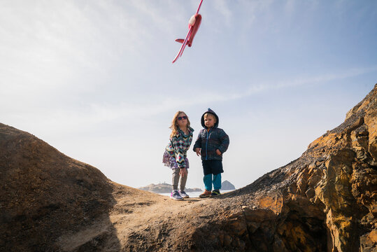 A boy and girl throw a toy plane off rocks at beach