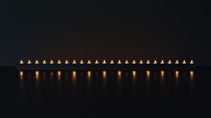 Fototapeta premium A row of lit candles arranged symmetrically against a pitch-black background, creating a serene, minimalist scene